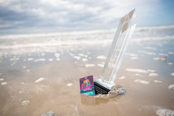 Boost on the Beach trophy and competitor's badge in the sand.